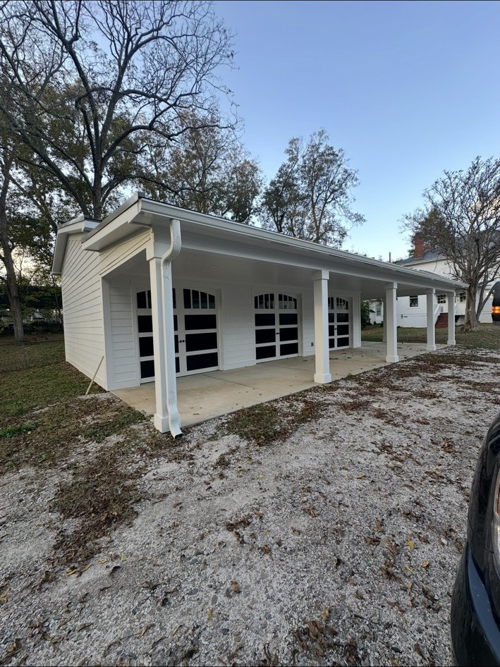 Finished white detached garage with covered perimeter and black-window garage doors